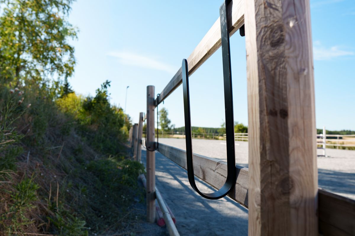 Två bomkrokar monterade på ridbanans staket, sedda från sidan