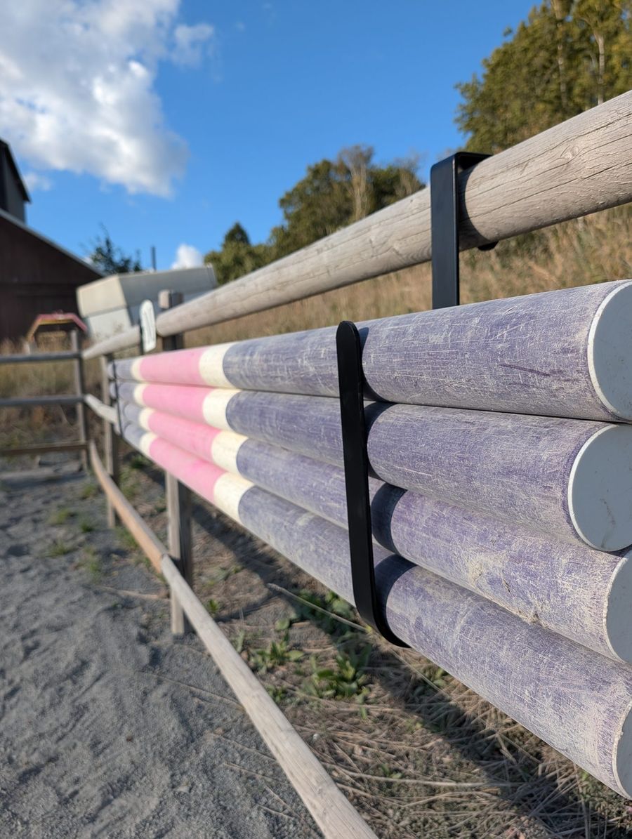 Fyra hinderbommar upphängda i Bomkroken på ridbanans staket